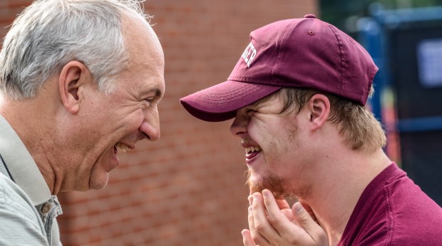 Man looking at and smiling at man with Down Syndrome wearing a red cap