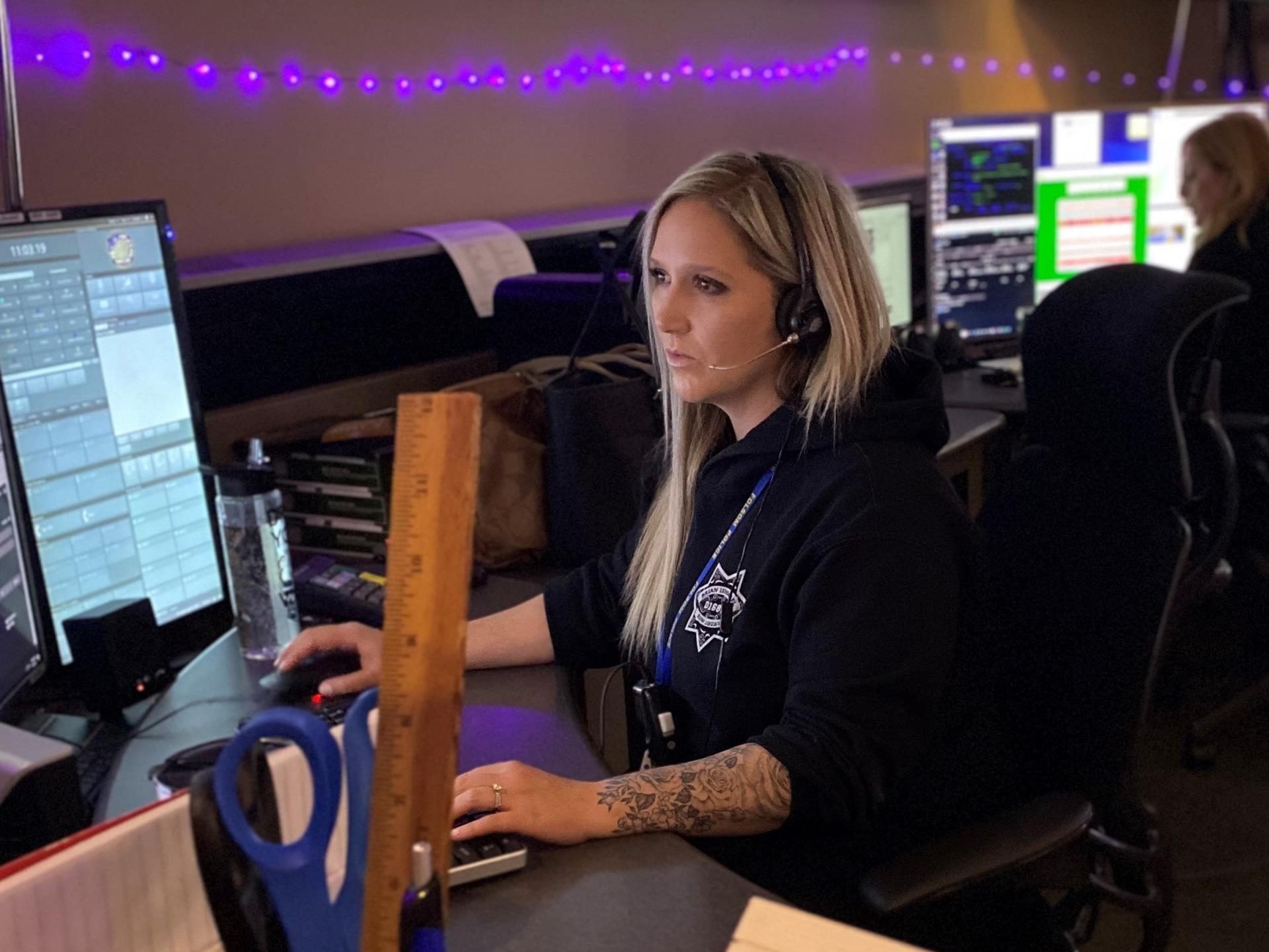 Photo of Dispatch Officer taking an emergency call while looking at the computer screen, wearing a black police sweatshirt