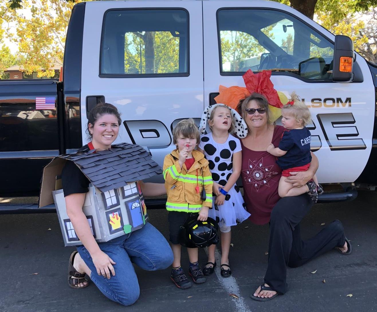 Family dressed in Halloween Costumes- Mom dressed as a house. Young boy as a fireman. Young girl dressed as a Dalmatian. Grandmother dressed as flames holding a baby not in costume.