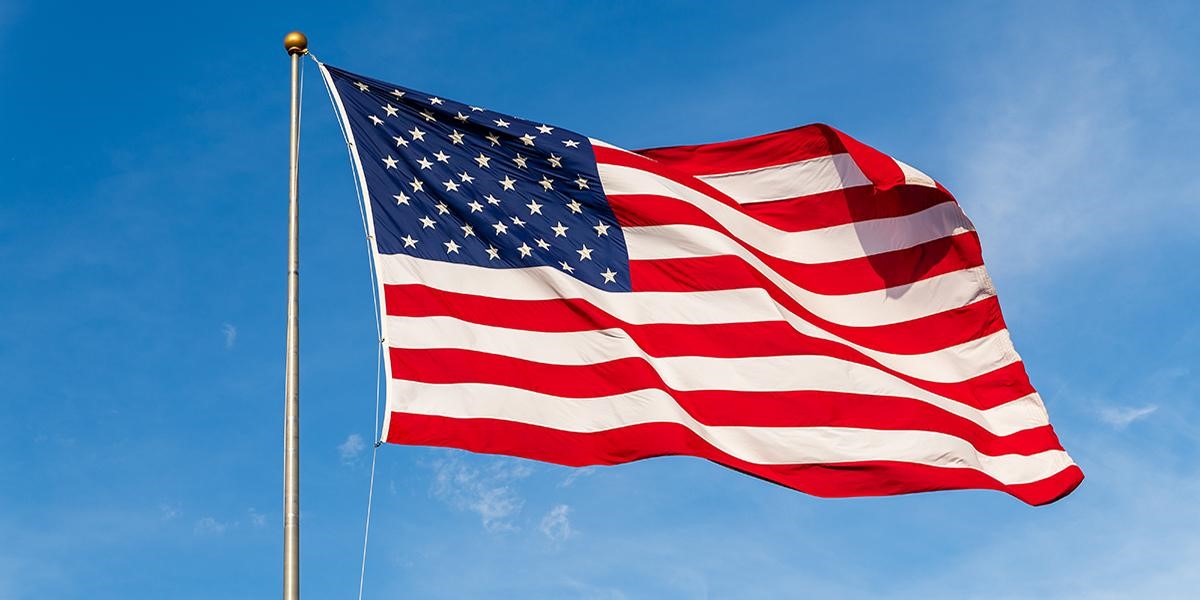 cof vet day photo of the american flag blowing in the wind in front of a clear blue sky