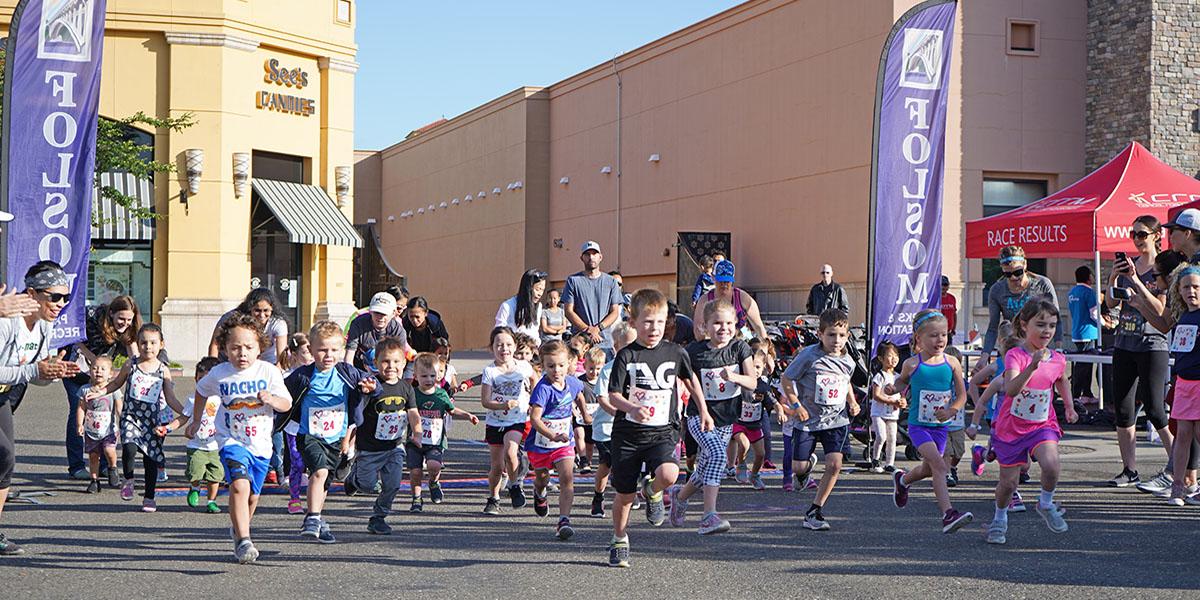 Love My Mom Kids Race Start at the Palladio in front of See's Candies with several kids starting the race with parents cheering them on the sidelines with a blue sky and two Folsom flags in the background