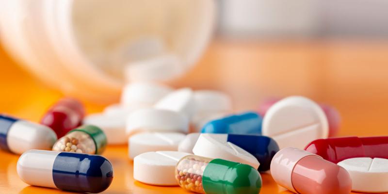 drugs and various pills outside of a bottle on an orange counter