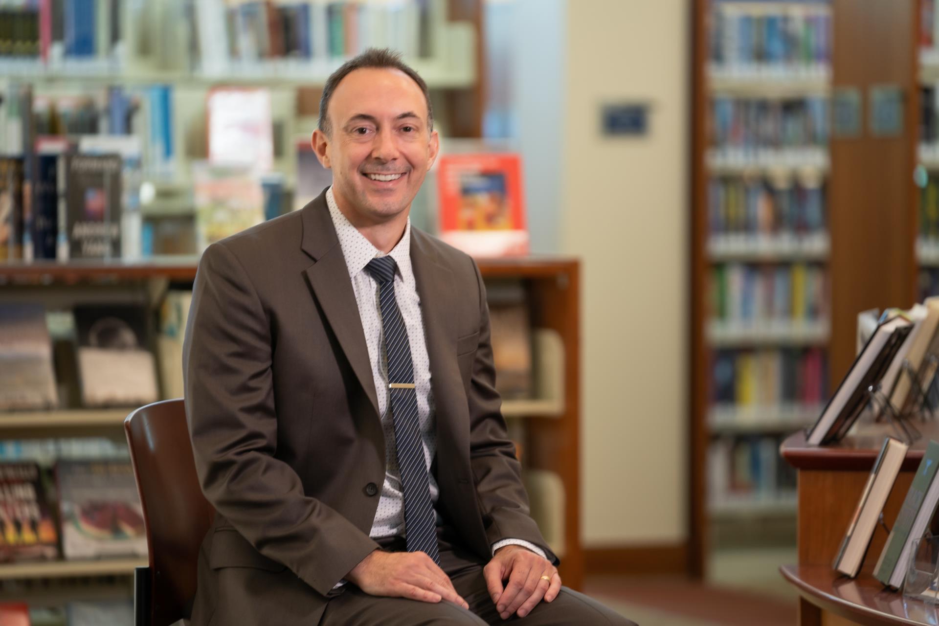 Library Director Thom Gruneisen sitting in the library in front of books