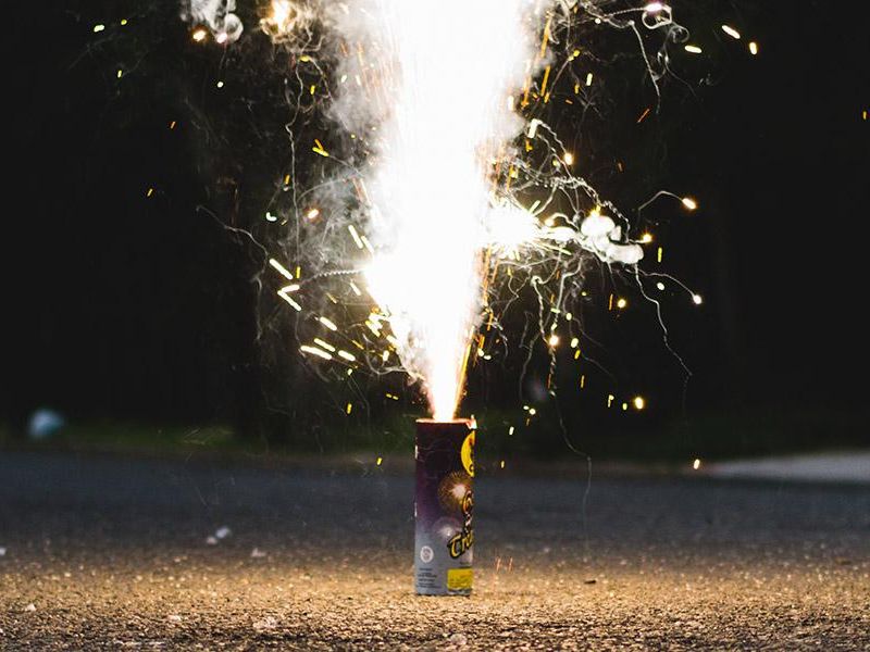 A small firework canister releasing bright sparks and smoke on a street at night.