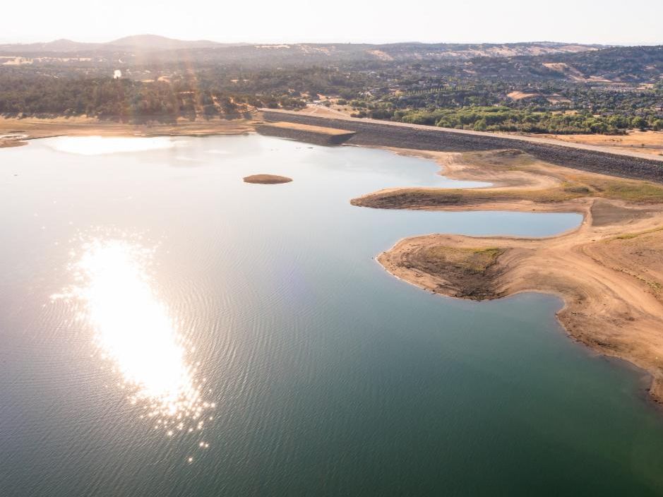 Aerial view of Folsom Lake with low water levels and exposed land during the 2021 drought, with the sun reflecting off the water.