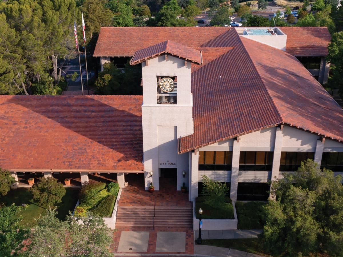 An aerial view of a brick building with a clock tower, surrounded by trees and pathways, representing City Hall.