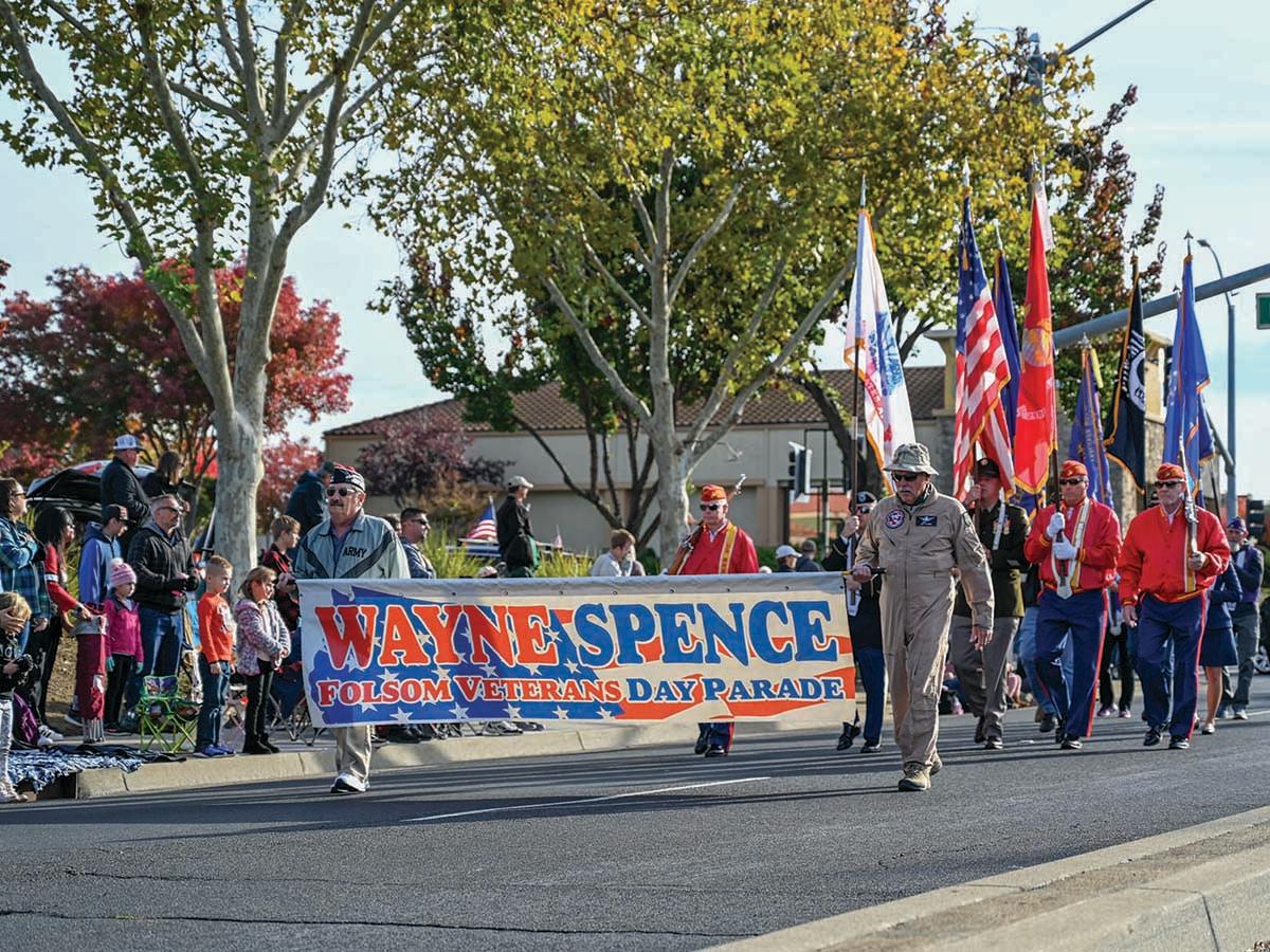 People marching in a parade, led by individuals holding a banner that reads 