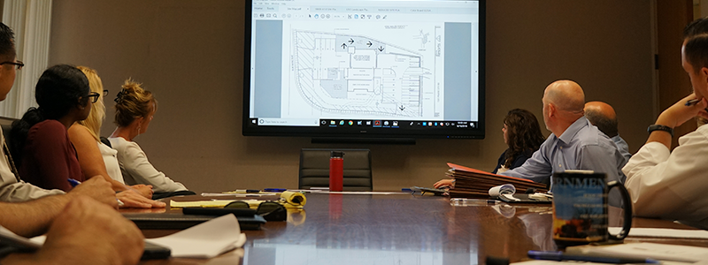 PLANNING SERVICES PAGE - docs and imgs. Table full of employees looking at a large planning map on the screen